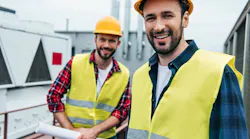 smiling engineers in safety vests and helmets with blueprint on roof By LIGHTFIELD STUDIOS - Adobe Stock