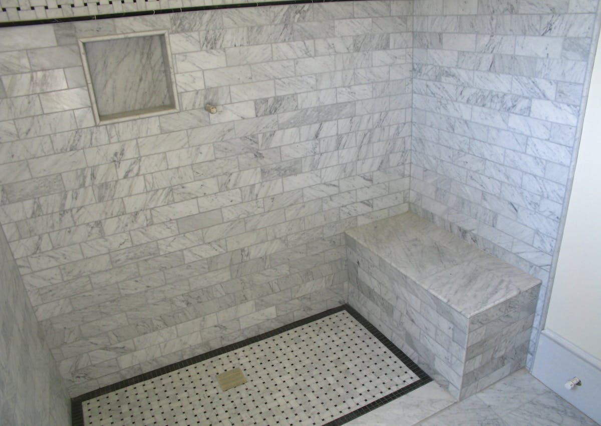 In the case of custom showers, such as this curbless example, the shower pan tends to be fabricated on site and finished with ceramic tile or a similar hard-surface material, such as the marble tile shown here.