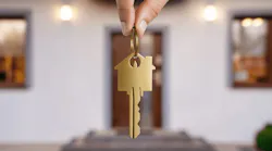 Hand holding house key in front of new home