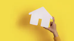 Hand holding white paper house in front of yellow background