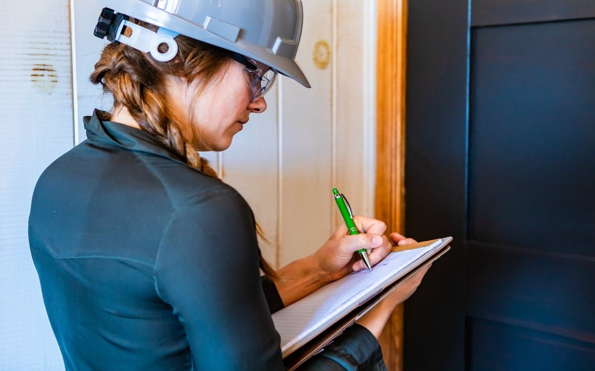 A woman in a gray hard hat takes notes at a jobsite