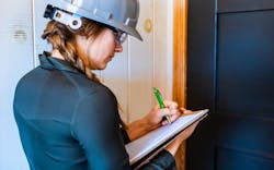 A woman in a gray hard hat takes notes at a jobsite A woman in a gray hard hat takes notes at a jobsite