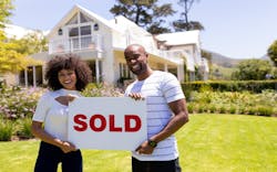 A couple stands in front of their newly purchased home, smiling and holding up a sign that reads 'Sold.' A couple stands in front of their newly purchased home, smiling and holding up a sign that reads 'Sold.'