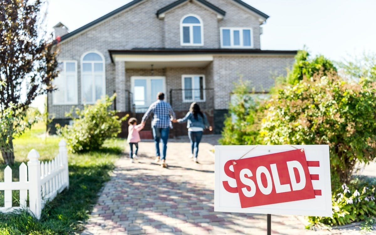 A family holds hands, running toward a single-family home with a 'Sold' sign in the front yard