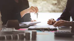 A selling agent hands over the keys to a buyer as they fill out paperwork