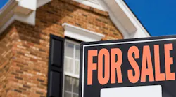 A 'For Sale' sign sits in the front yard of a brick single-family home