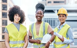 Three young women stand at a construction site wearing yellow vests Three young women stand at a construction site wearing yellow vests