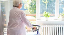 An elderly woman stares out the window of her home