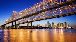 A bridge in New Orleans is illuminated at night with the city skyline behind it