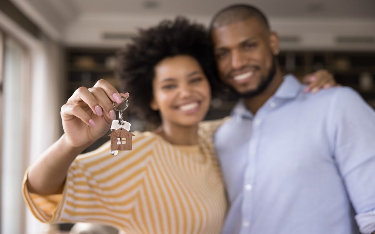 A Black couple smiles while holding up keys to their new home