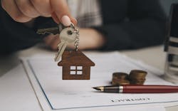 A real estate agent hands over a house key to a buyer. A contract with a pen on the desk indicates the contract was recently signed. A real estate agent hands over a house key to a buyer. A contract with a pen on the desk indicates the contract was recently signed.
