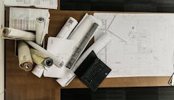 rolls of floor plans on wood desk with laptop rolls of floor plans on wood desk with laptop