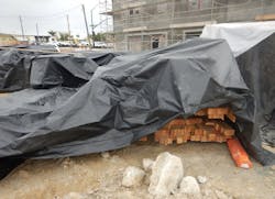 lumber on jobsite covered by plastic tarp for protection from weather lumber on jobsite covered by plastic tarp for protection from weather
