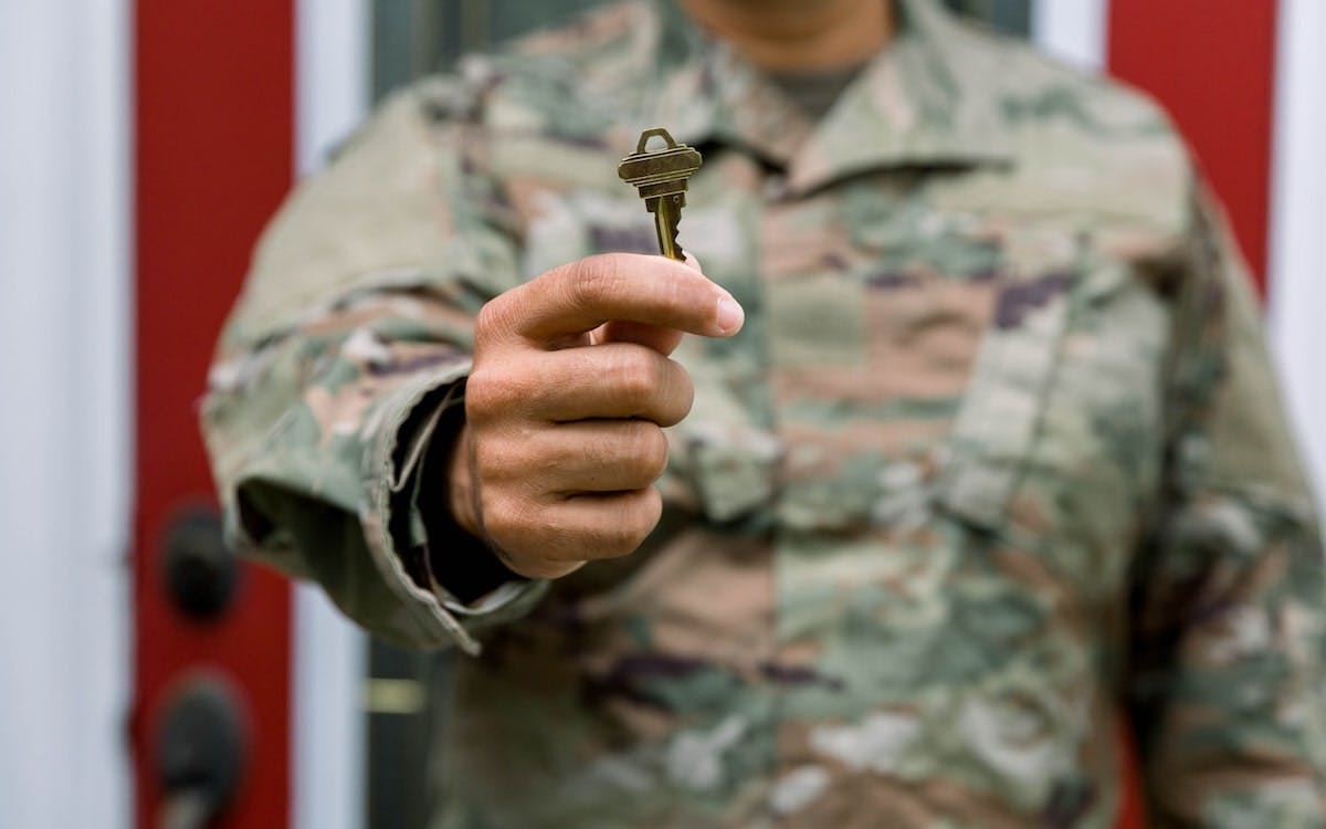 A man in a U.S. Army uniform holds up a key to a new home