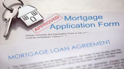 A mortgage loan application with a stamp of approval and a set of house keys on top of it