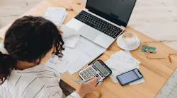 A renter looks over budget with laptop, bills, and calculator at a table