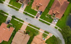 Aerial view of a residential street in a suburban neighborhood with green lawns. Aerial view of a residential street in a suburban neighborhood with green lawns.