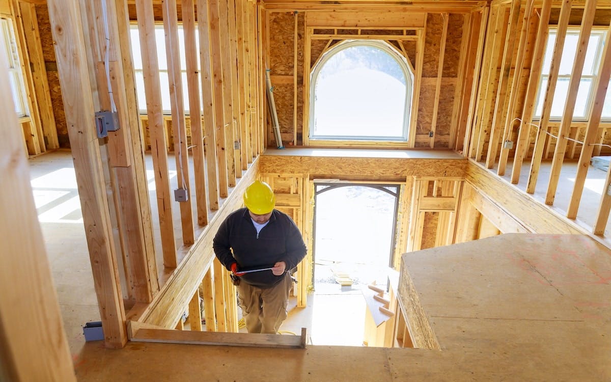 A contractor walks up the stairs in a partially constructed home