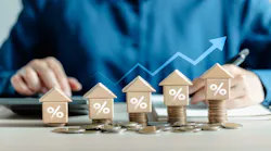 A person places model homes with percentage symbols on them on top of stacks of coins. From left to right, the coins increase in height, reflecting rate increases.