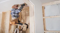 A construction worker stands on a ladder to get closer to ceiling dry wall.