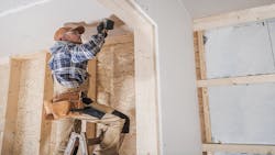 A construction worker stands on a ladder to get closer to ceiling dry wall. A construction worker stands on a ladder to get closer to ceiling dry wall.