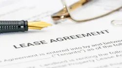 A close-up of a lease agreement with a pair of glasses and a pen sitting on top of them.