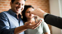 A smiling couple takes house keys from a real estate agent after purchasing their home.