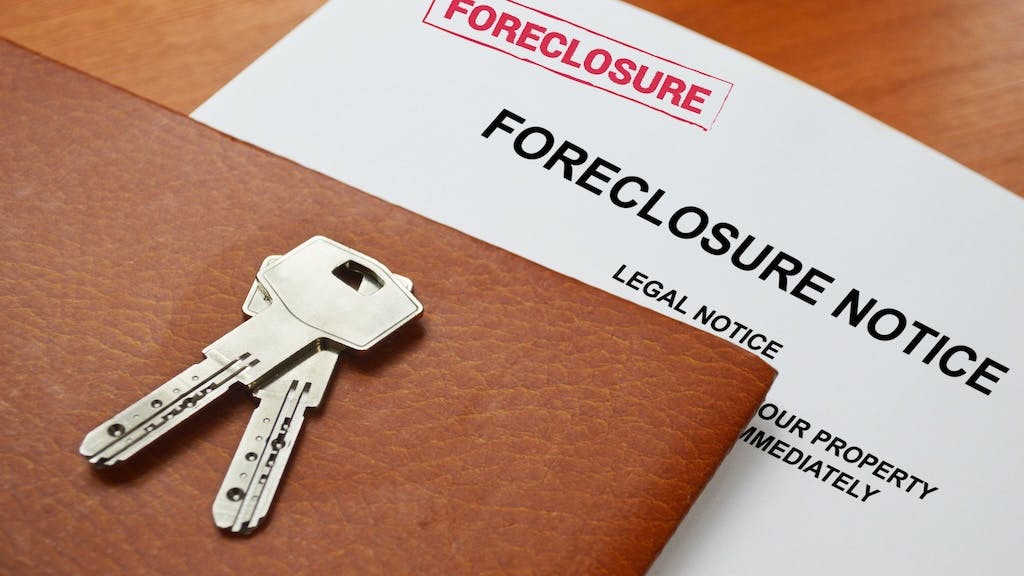 Closeup of a foreclosure notice with a leather folder and house key sitting on top