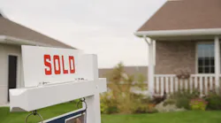 A white sign with the word 'sold' on it sits in front of a single-family home