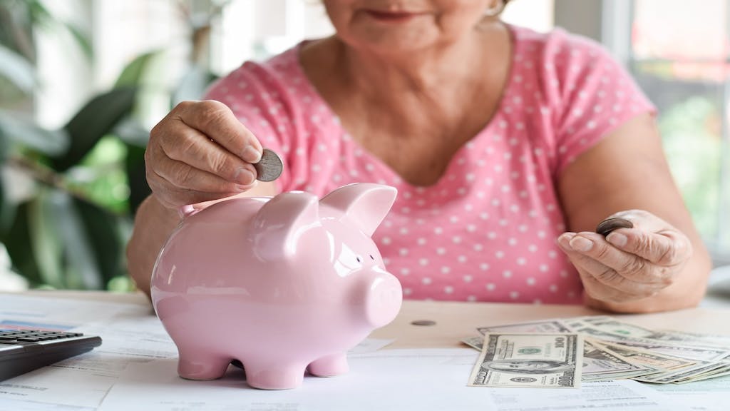 An older woman puts coins into a pink piggy bank