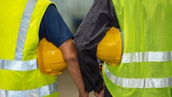 Two construction workers wearing reflective vests and carrying hard hats Two construction workers wearing reflective vests and carrying hard hats