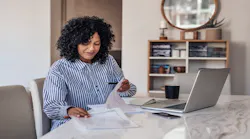 A remote worker looks over notes with her laptop open on the table in front of her.