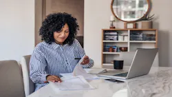 A remote worker looks over notes with her laptop open on the table in front of her.