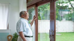An elderly man looks out the window of his home to the backyard. An elderly man looks out the window of his home to the backyard.