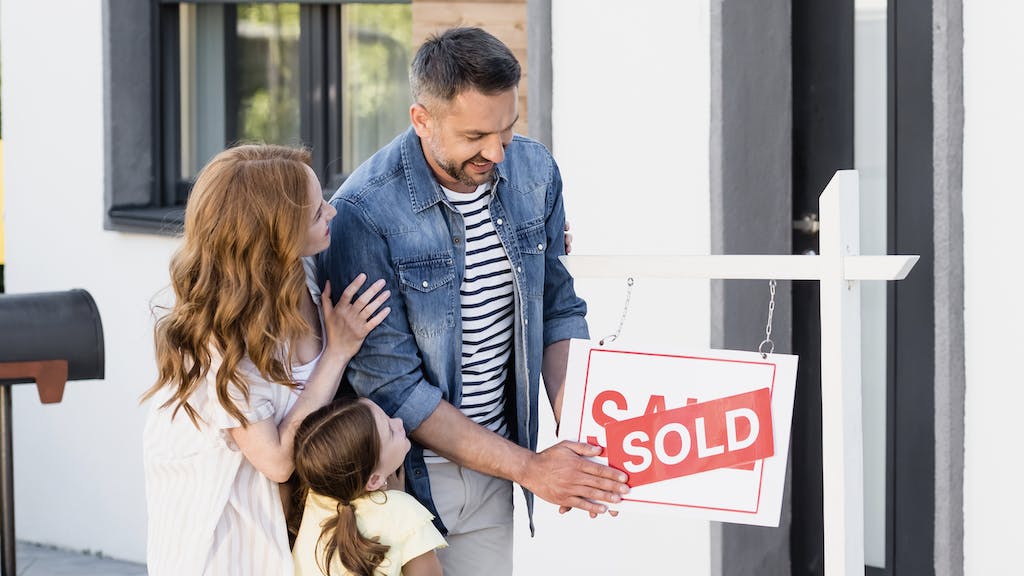 A family puts a 'sold' sign over a 'for sale' sign in front of a new home