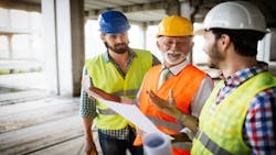 Three construction workers in yellow vests and hard hats discuss plans at a jobsite. Three construction workers in yellow vests and hard hats discuss plans at a jobsite.