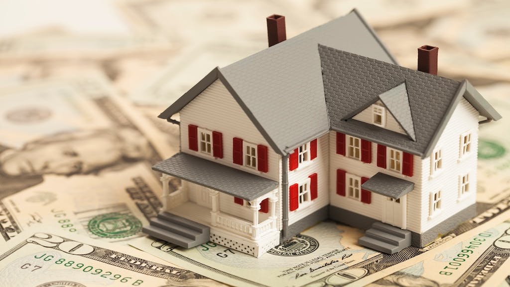 A model home sits on a pile of $20 bills