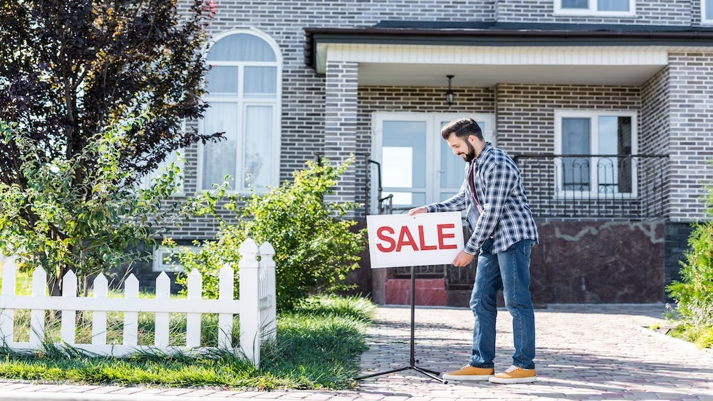 A man puts a 'Sale' sign outside his home