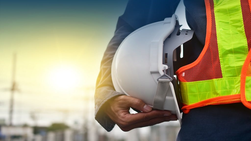 A construction worker in a safety vest holding a hard hat