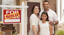 A couple with their daughter stand in front of their home with a 'sold' sign