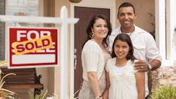 A couple with their daughter stand in front of their home with a 'sold' sign A couple with their daughter stand in front of their home with a 'sold' sign
