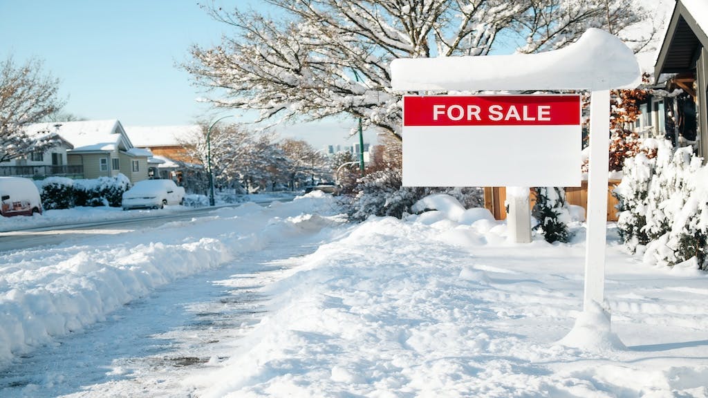 A snow-covered yard with a red 'For Sale' sign