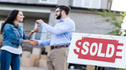 A woman shakes hands with real estate agent after purchasing a home. A 'sold' sign stands in front of them.
