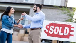 A woman shakes hands with real estate agent after purchasing a home. A 'sold' sign stands in front of them. A woman shakes hands with real estate agent after purchasing a home. A 'sold' sign stands in front of them.