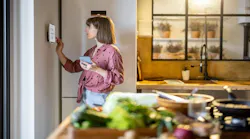 A woman adjusts settings on smart thermostat.