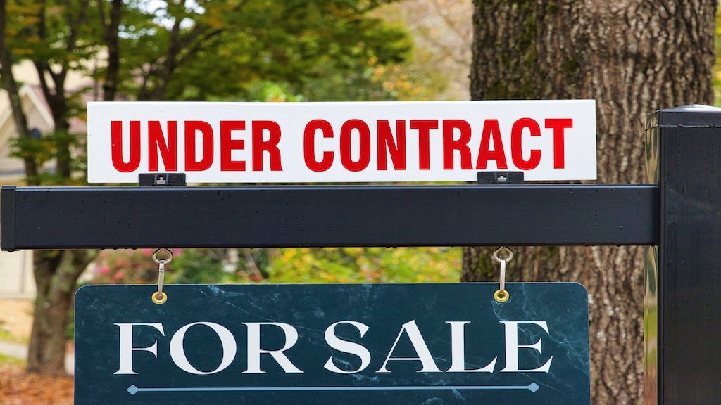A closeup of a 'For Sale' sign with a sign above it reading 'Under Contract.'