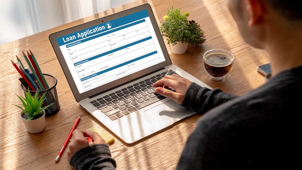 An individual fills out a loan application form on their laptop