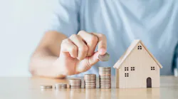 An individual stacks coins in ascending order. After the rows of coins sits a model home, indicating the rise of housing costs.