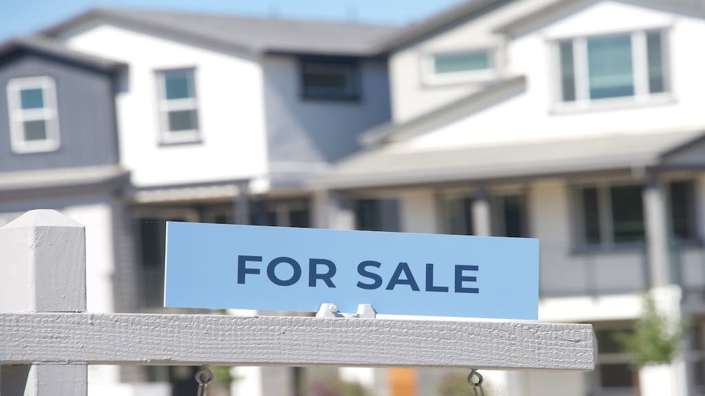 A closeup image of a 'For Sale' sign in front of a new home