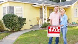 Homeowners stand in front of their home with a 'For Sale' sign Homeowners stand in front of their home with a 'For Sale' sign
